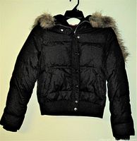 Front view of black DKNY jacket with fur attached on hood showing puffer material, zip and snap closure, ribbed cuffs and waistband.