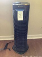Front view of the black Honeywell air purifier showing brand and general condition, with its power cord outstretched on the floor.