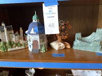 Shelf containing a Dept. 56 ceramic church music box, detailed castle sculpture, ceramic tree on stone base, and ceramic Great Wall of China sculpture