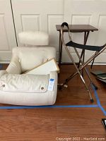 White bed rest pillow with arms, matching leg rest pillow, folding bed tray, and folding seat shown together on wood floor.