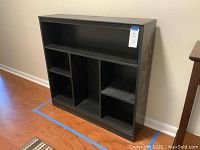 Front view of black painted bookshelf with multiple compartments and gold bamboo motif on side panels.