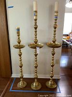 Photo of three oversized brass candle stands of varying heights grouped together, showing overall design and scale