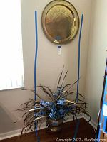 Photo showing the brass plate hanging on wall above the brass planter with silk plant arranged inside