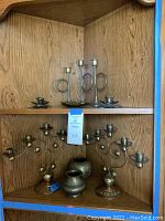 Full view of wooden shelf with displayed brass decor including candlesticks, candelabras, and small vases.