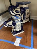 Two blue and white ceramic elephants on wooden floor with tape marking around them, showing both short and tall elephant