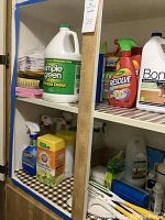 Shelf with various cleaning liquid bottles including Simple Green all-purpose cleaner, Resolve fabric cleaner, Bona hardwood floor cleaner, disinfecting wipes and cleaning sprays.