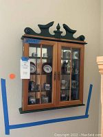 Full view of decorative wooden wall cabinet mounted on wall showing general size and style with glass-front doors.
