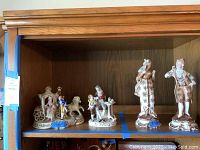 Shelf displaying the porcelain colonial-style figurines arranged, including horse carriage with figures and two standing colonial characters.