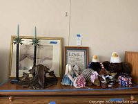 Full view of shelf showing framed wall art, candle holders, bald eagle figurines, cloth dolls, and music boxes