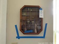 Front view of wooden octagonal mini collectible wall case mounted on the wall, glass door closed, showing small collectible items inside.