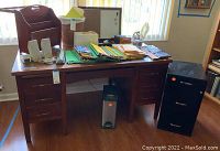 Wide view of large wooden desk with file folders and file cabinet beside it and waste bin underneath
