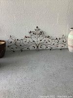 Photo of metal wall hanging with leaf and vine scroll pattern leaning against wall next to ceramic pots