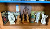 Shelf view showing the full collection of religious decor items including statues, artwork, urn, and pillow.