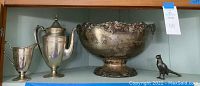 Wide view of silver plated tea set, decorative bowl, and bird figurine on shelf