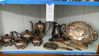 Full view of all silver plated items including coffee pot, teapot, creamer, sugar bowls, serving tray, hand mirror, and brush.