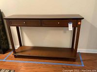 Full view of sofa table showing top, legs, drawers, and lower shelf on hardwood floor.