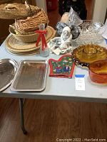 Overview of lot including wicker placemats and baskets stacked, clear and amber glass bowls, metal serving platters, ceramic decorative items, chopsticks, and kitchen festive decor