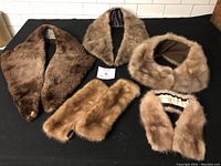Lot of six decorative fur coat pieces laid flat on a black surface; mix of 5 mink pieces and one unknown fur in shades of brown.