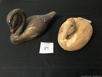 Photo showing two duck decoys on a black surface, one dark brown with yellow paint wear and repair on neck, one light natural wood decoy.