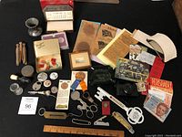 Lot of mixed collectible and utility items spread on table: pins, badges, coins, thermometer, small scale, pocket cutter, glass ashtray, paper memorabilia, wooden ruler.