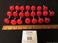Photo showing 22 red round drawer pulls laid out beside a ruler for scale, showing approximately 1.5 inch size.