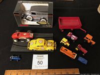 Wide shot showing all 11 toy vehicles including boxed Sears Craftsman vintage car in packaging, red wagon, two slot cars on track, and smaller vehicles including tractors and trucks.