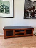 Front view of cherry wood electronics credenza with black glass top and doors, showcasing the overall shape and design.
