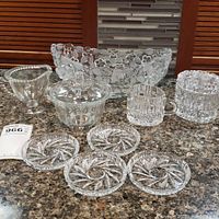 Photo showing the large floral crystal bowl, crystal creamer and sugar bowl, smaller bowl, and set of four crystal coasters arranged on a countertop.