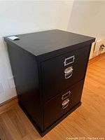 Front view of black 2-drawer filing cabinet showing metal pull handles and label holders.