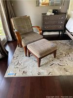 Photo showing beige floral rug under chair and ottoman on dark hardwood floor.
