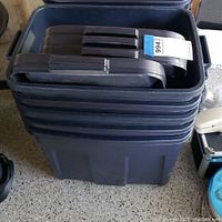 Stack of nine large dark gray plastic storage bins with lids stacked inside each bin for compact storage.