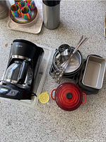 Wide view of the lot displaying the coffee maker, baking pans, skewers, and Le Creuset Dutch oven on a countertop.