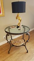 Full view of round glass top table with gold abstract lamp and small decorative items on top.