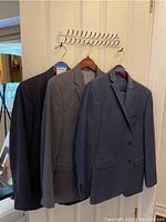 Three men's suit jackets on hangers showing dark navy and gray colors
