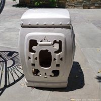 Front view of white ceramic side table with ornate cutout designs and raised circular accents along the top edges, set on outdoor patio floor.