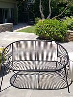 Front view of black rope-style metal loveseat on stone patio