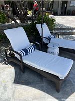 Pair of dark brown wicker chaise lounges with white cushions and blue/white striped bolster pillows next to a pool area.
