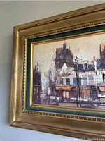 Close-up of the painting showing detailed brushwork of buildings and street elements, with gold and green frame visible.