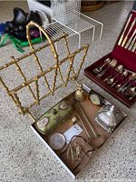 Overview of vintage items including gold-tone bamboo magazine holder, green china jewelry box, silver clock, vintage silverware set in wooden box, metal dog coasters and gold lady bell.