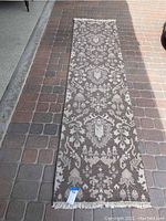 Full view of the brown and beige vintage runner rug placed on a paved surface, showing the overall design pattern and fringed ends.
