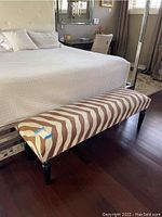 Angle view of zebra patterned upholstered bench at foot of bed on dark hardwood floor.