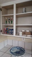 Cabinet shelf with three tulip-shaped art glass vases, two drink cans, two clear cordial glasses, Wedgwood china pieces and Delft platter on counter