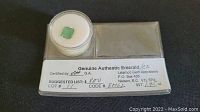 Top-down view of rectangular green emerald in clear round plastic case with white foam insert