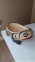 Side angle view of carved wooden frog bowl showing painted stylized design