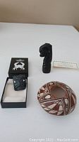 Photo of all three Native American art pieces: a Navajo pottery bowl, a black carved rectangular sculpture, and a black carved horse head sculpture with damage