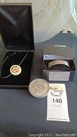 Photo of silver wolf bracelet in black box, silver circular pendant necklace in open black box, and round silver token.