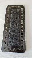 Front view of dark wood cribbage board with central Native art style carving and surrounding scoring holes with yellow numbering.
