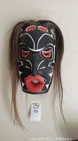 Frontal view of full mask hanging on white wall with long hair around sides.