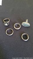 Five sterling silver rings on black fabric background, showing overall lot contents