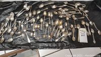 Full spread of approximately 50 assorted sterling spoons and one fork on black background